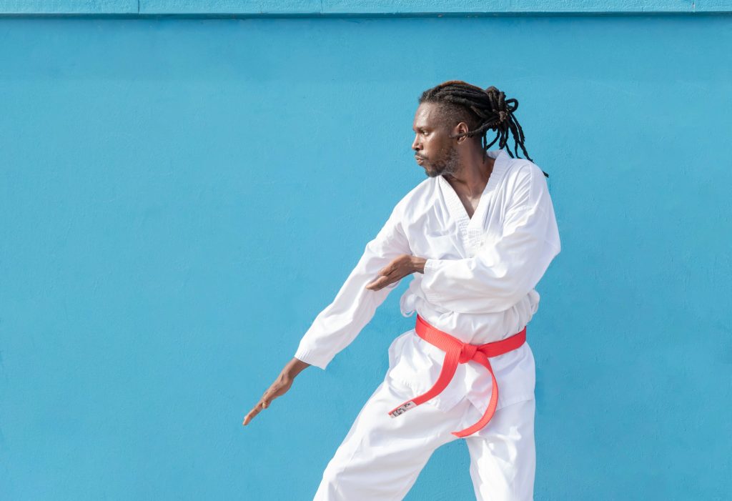 a young african american man training taekwondo outdoors on a blue background